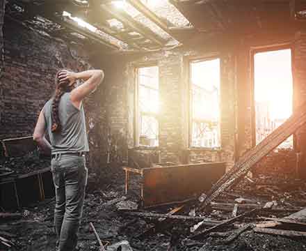 Person standing in burnt, damaged room, looking outside.