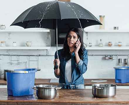 Woman holding umbrella inside, leaking roof issue.